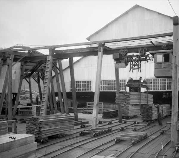 Elevated view of a monorail hoist, lumber carrying unit, and monorail track switch at the Port Hammond Lumber Company. Men are working with stacks of lumber on small wheeled carts on tracks.
