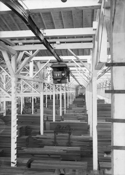 Elevated view of monorail hoist with lumber carrying unit, with the number 17 painted on the front, at the Port Hammond Lumber Company. Men can be seen in the lower background working on the floor of the building.