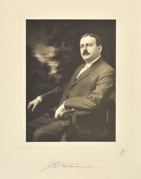 Three-quarter length seated studio portrait in front of a painted backdrop of James D. Mortimer, New York company president.