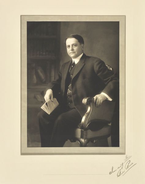 Three-quarter length seated studio portrait in front of a painted backdrop of Peter Reiss, Sheboygan merchant.