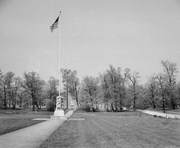 Flag pole with limestone carving of women and men by Alonzo Hauser, who was appointed by the Farm Security Administration, at its base. The sculpture was begun in 1938 and finished and dedicated on the 4th of July in 1939. The sculpture on building in background is also by Hauser.