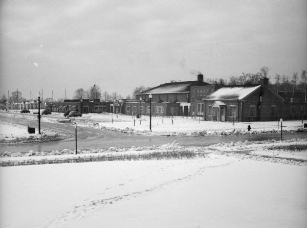 Commercial buildings, roads, cars parked in lots, as seen from the snow-covered lawn of the Village Hall.