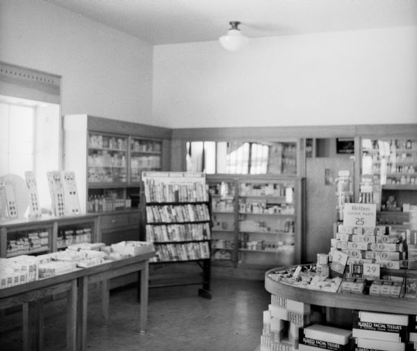 Interior of the community drugstore. Visible products include "Klenzo Facial Tissue," "Briten Toothepaste" and "Kleenex Tissue."