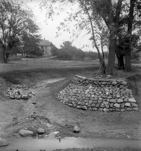 Rocks placed to control the flow of Dale Creek. A house is visible in the background. This picture was likely taken as a study of the water drainage in early Greendale.