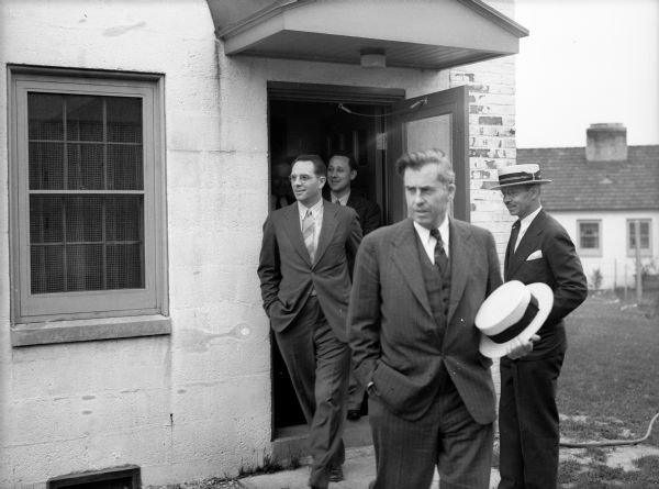 Henry Wallace walking out of a building with other men in the background. Henry Wallace, then the United States Secretary of Agriculture, visited and toured Greendale.