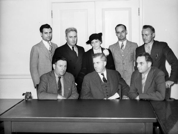 Henry Wallace, sitting at a table posing for a photograph with six men and one woman. Henry Wallace, then the United States Secretary of Agriculture, visited and toured Greendale.