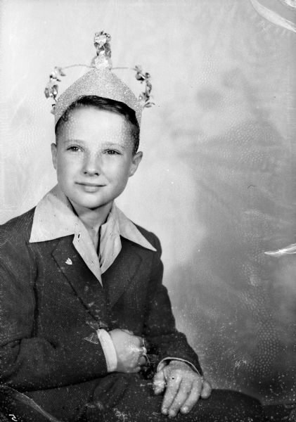A smiling young boy posing wearing a crown and a dress jacket. He is also wearing what is possibly a 4-H pin on his lapel.
