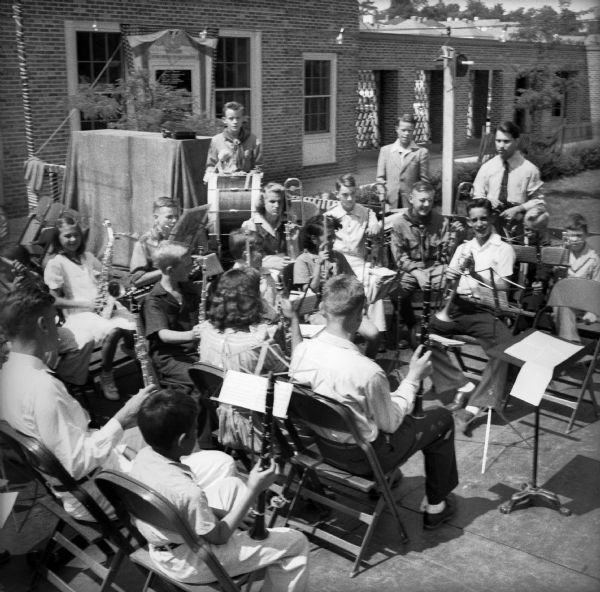 A group of boys and girls seated with instruments are waiting to perform music at a Civilian Defense Rally.