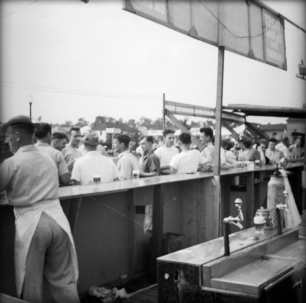 A view from behind the bar of a Civilian Defense Rally. Men and women are lined up and taps are visible.