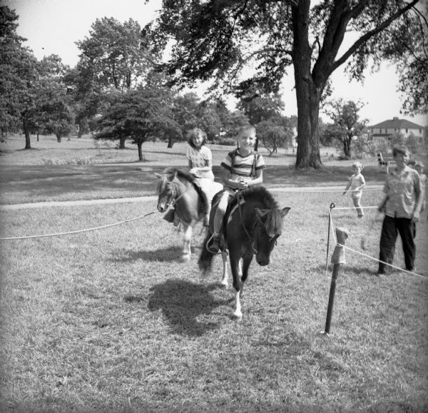 Children riding ponies in a roped-off area in a park at a Civilian Defense Rally.