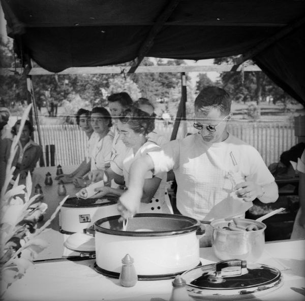 Women and men preparing hot dogs in crock pots at a booth at the Civilian Defense Rally.