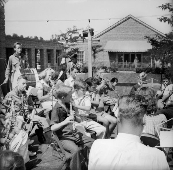 A group of school-age children with a few adults playing band instruments outdoors at a Civilian Defense Rally.