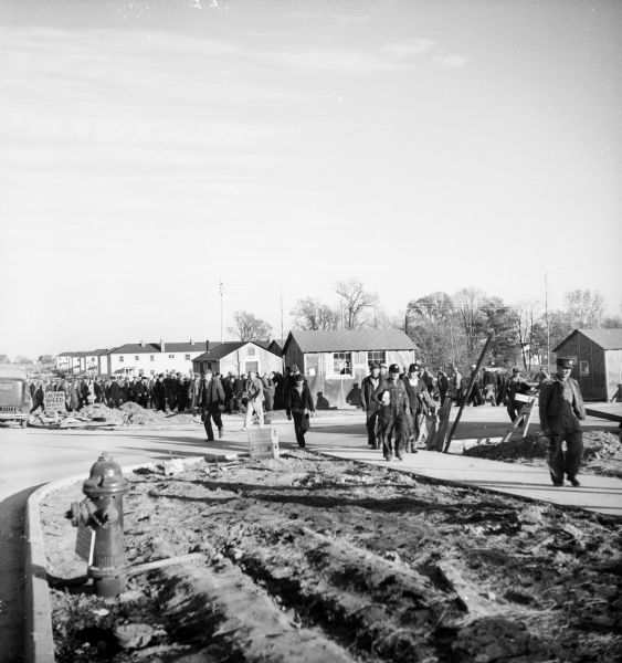 Large group of construction workers walking through neighborhood of houses that are in the middle of being constructed.