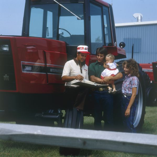 Color photograph of a salesman meeting with a customer's family next to an International Harvester 3688 tractor at a dealership. The photo appears to be staged for advertising or publicity purposes.