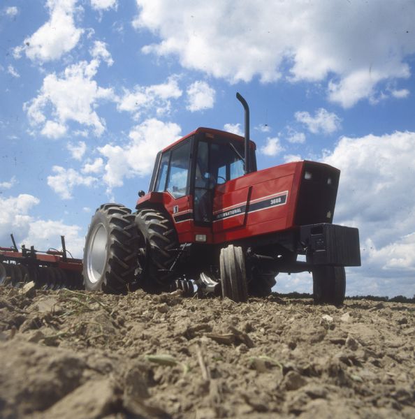 Man driving International Harvester 3688 tractor with disk in field.