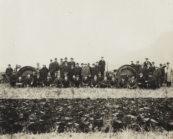 Two La Crosse Happy Farmer tractors in a field with a large group of men wearing coats and hats. The men are possibly La Crosse Tractor Company executives.