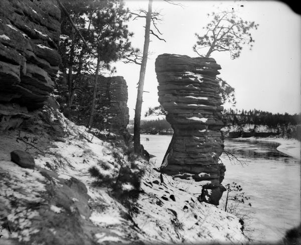 A winter view of Chimney Rock at the Dells. There is snow on the ground and ice on the river.