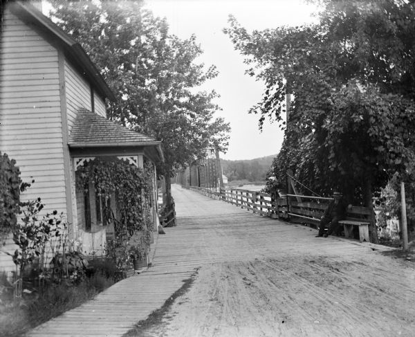 Wagon toll bridge. There is a building on the left, and a man is sitting on a bench on the right side of the road leading onto the bridge.