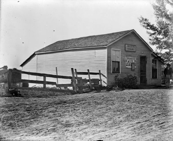 Exterior view of a post office. Sign near door says: "Post Office. Sandusky." A man stands just outside the door, looking at another man standing inside.