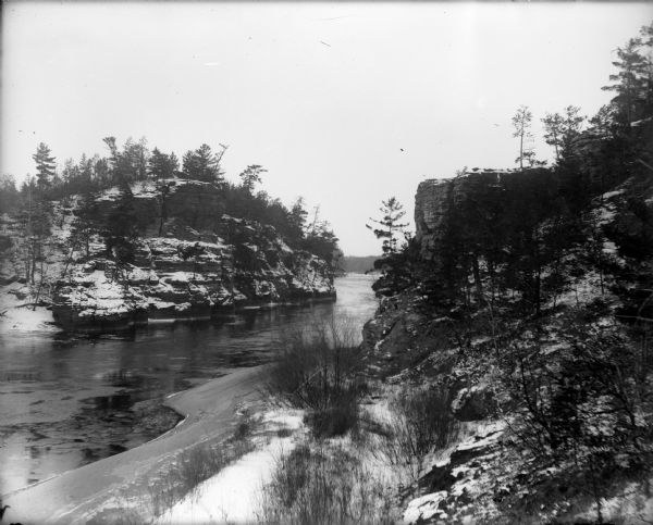View from bank of the Wisconsin River of the Jaws of the Dells in winter. Snow is on the ground and ice lines the shoreline.