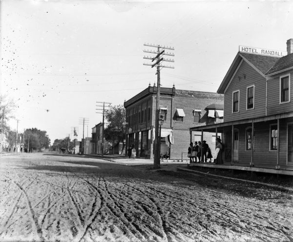 View from road of buildings in North Freedom. Hotel Randall is in the right foreground. A group of young women and others have gathered on the porch of the hotel. Several utility poles and wires are visible along the sidewalk.