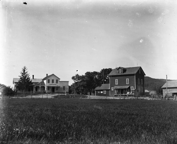 Exterior view across field of mill and store at Black Hawk. There are feed sacks on the porch of the mill, and a horse is on the far right.