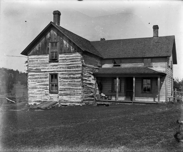 The home of Carl L. Buelow, a combination of a log and frame house, also used as a saloon. A rod at the left corner can be used to hang a sign. A chair sits on the porch.