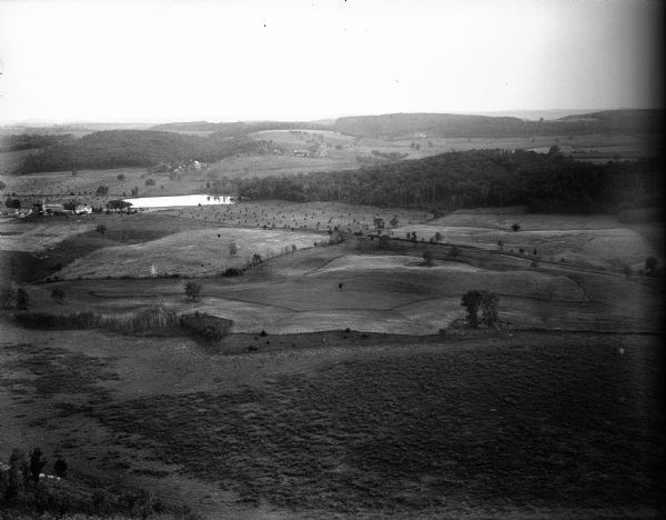 The view from Gibraltar Rock across farm fields and woods.  There are corn shocks in several of the fields. A farm house and outbuildings stand near a pond.