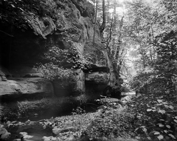A view of a ravine showing rock strata and a stream.