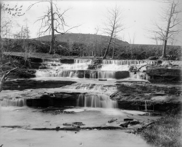 View of Skillet Falls from downstream. The trees are bare, and tree stumps are visible on the hill in the background, known locally as Mount Baldy.