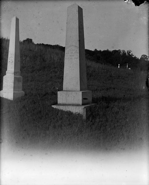 A stone obelisk marks the grave of Jonas Tower in a country cemetery.  A smaller obelisk stands to the left, and other grave markers can be seen in the background.