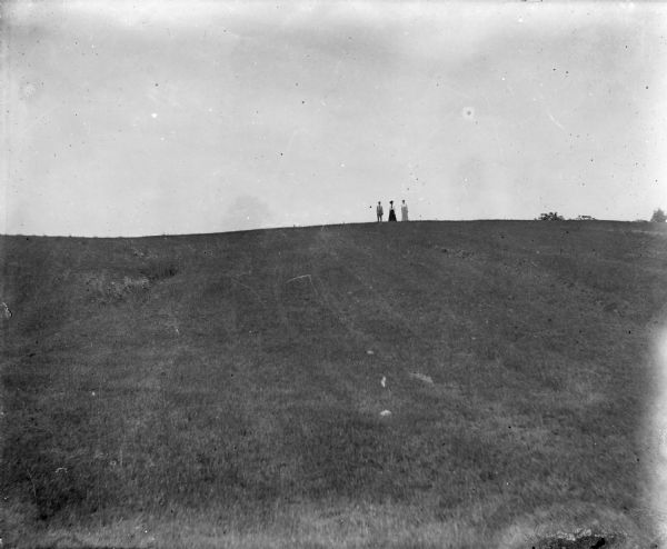 Two women and a man stand in the distance on the crest of a grassy rise.