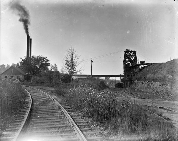 Iron mines with railroad tracks three miles south of North Freedom, in La Rue. One the left are buildings with three large smokestacks; on the right is machinery for loading train cars.