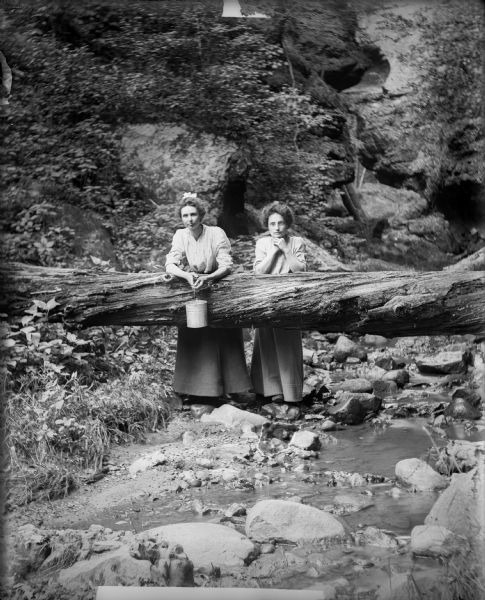 Two women pose behind a log which has fallen across the stream in Parfrey's Glen. One woman holds a small pail.