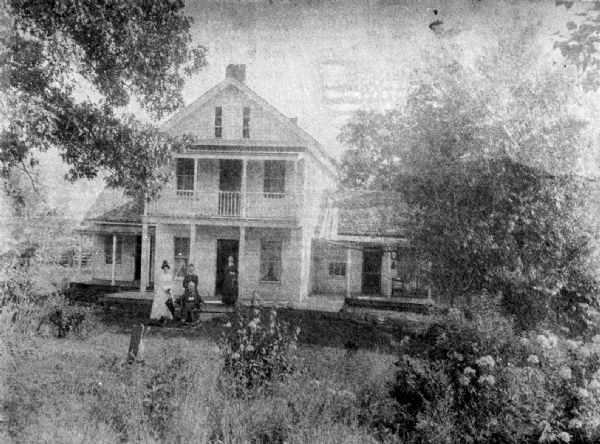 A copy of an old photograph of the W. McAuley Halfway House, an inn between Prairie du Chien and Viroqua. Mr. McAuley sits on a chair while a granddaughter, a daughter, and his wife stand.