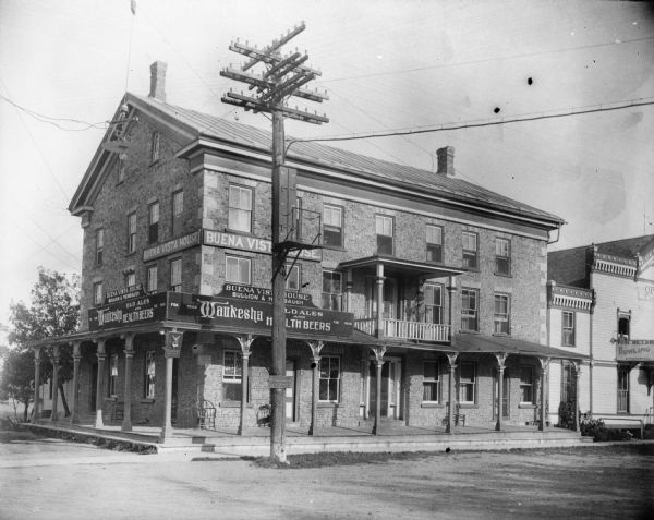 View from road of the Buena Vista House. There is a utility pole in front with many wires attached. This Greek revival inn was erected in 1843 by Samuel R. Bradley of Milwaukee, who is said to have gathered personally all of the cobblestones used in its construction. He and his wife managed the inn from its opening in the late 1840s until about 1851.