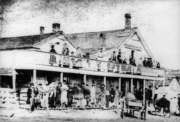 This view of the Token Creek Tavern (Field's Inn) was created from a tintype (circa 1870) by E.E. Lawrence. A crowd has gathered on the porch and balcony of the wooden structure. There is a horse-drawn wagon in front and a barn in the background.

Marcus H. Wheeler, father of Ella Wheeler Wilcox, is on the upper balcony playing his violin. The sign on the hotel reads, "Fleishbein & Kelley."
