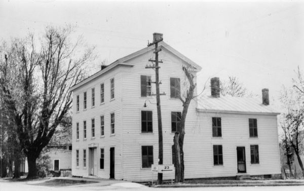 Exterior of the White House Inn, a three-story wooden structure with a two-story wing in the rear. A road sign for Highway 23 is in the foreground on the corner near a large utility pole.