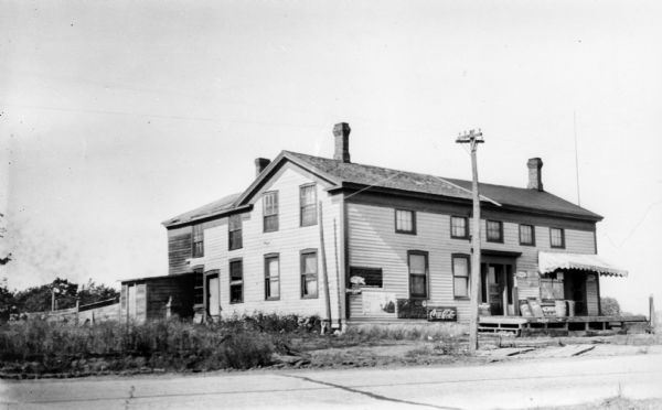 An old commercial structure identified as the Twin Island House. There are feed sacks on the  porch and a Coca-Cola sign on the front of the building. This appears to be the same structure identified as the Guenther Half Way House.