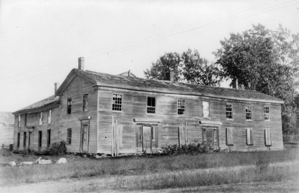 Steele Tavern, built in 1849. The large, two-story wooden building with a rear wing, is in a state of neglect. The portion on the left has twelve over eight windows; the right has six over six windows.  Many of the first floor windows have been boarded over.