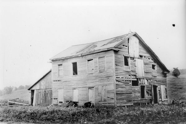 A wooden, two-story saltbox style building in an advanced state of neglect.