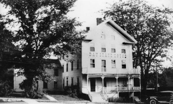 View from across street of three-story, classical revival, Bay State House. There is a side wing and a two-story porch across the front. An automobile is parked to the right near a utility pole.