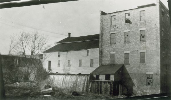Old stone mill, with a smaller wooden addition on the left. Water is passing through the flume.