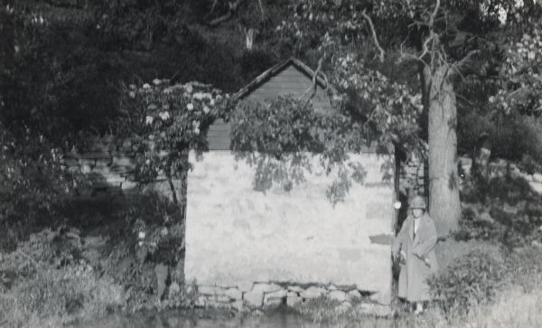 An unidentified woman stands beside a stone spring house at a spring between Mt. Horeb and Black Earth.