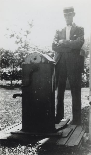 Charles E. Brown stands beside a chain and crank operated water pump. Brown was the curator of the museum of the State Historical Society of Wisconsin and president of the Wisconsin Archeological Society.