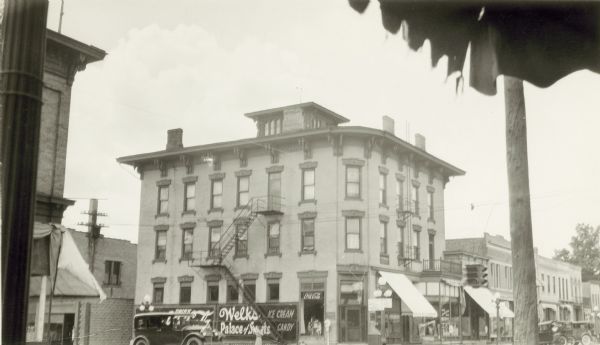 The brick, Italianate style Fox House hotel in Columbus. There are brackets under the overhang and a large belvidere. A sign on the building advertises Coca-Cola and "Welk's Palace of Sweets." There are automobiles on the street.