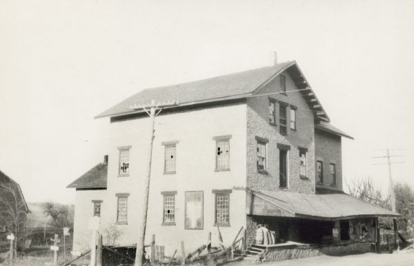 Three-story stone mill built in 1847 by J.C. Sherwood. Many panes of glass in the twelve over twelve windows are broken and the roof over the loading dock is sagging. The gable end of a barn is seen on the left.