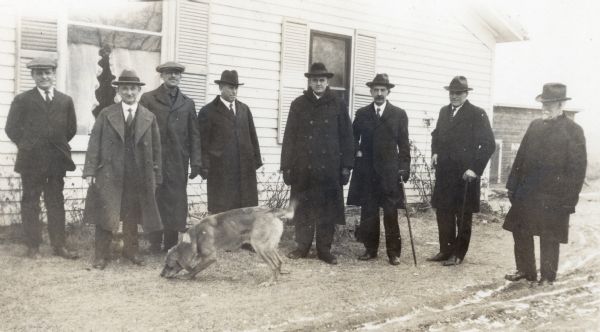 Eight men comprising the Heart of the Hills Walking Club, founded by H.E. Cole, pose with a dog beside a house. They are left to right, Harold Baldwin, T.F. Risley, M.C. Crandall, Rev. E. C. Henke, Rev. J.E. Kundert, H.E. Cole, J.H. Horstman, and R.B. Griggs.