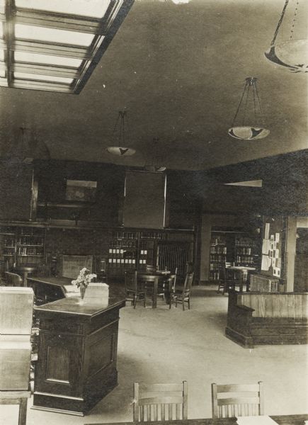 Interior view of the Columbus Library looking toward children's room. In the foreground is a reading table, and librarian's desk. There are also bookshelves, a fireplace, and a skylight.