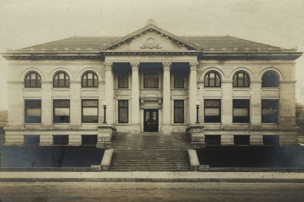 Exterior view of the Eau Claire Public Library. Note on reverse of image reads: "1904, Patton + Miller, Chicago, Cost $40,000." Over the main entrance it reads: "Eau Claire Public Library." The entrance has four Corinthian columns. The two-story facade has large arched windows.

Additional information from "Small Library Buildings; A Collection of Plans Contributed by the League of Library Commissions, 1908."
COST - $40,003.81. Contract $29,981.20 (including cork carpet and wall shelving). Tile roof $1,600. Gable ornaments $138. Steam pipes in gutters $42. Heating and ventilating $1,719, Electric wiring $5.22, Light fixtures $550, Plumbing and gas fitting $904, Shades $65, Decorations $810, Leaded glass $312, Architect's fees $1,884.66, Superintendence $384, Chairs $295, Catalogue drawers $69, Catalogue case, loan desk, tables and librarian's desk $728.